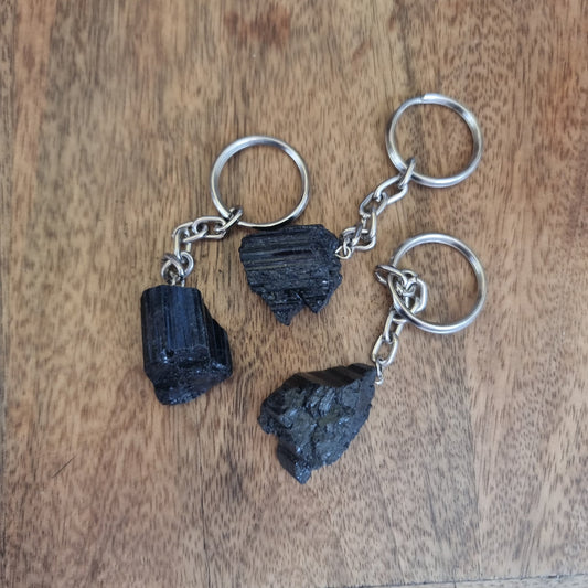 Three raw black tourmaline pieces on silver keyrings resting on a wooden table