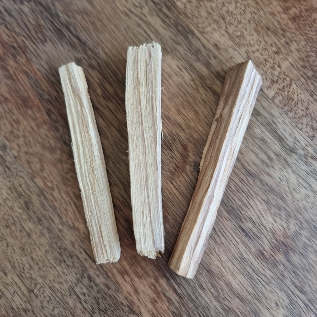 Three pale palo santo sticks lying on a dark wooden table