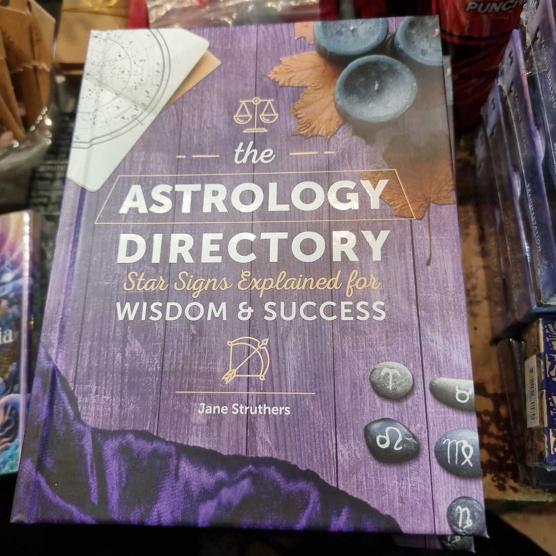 The Astrology Directory book by Jane Struthers on a Rivendell shop shelf, its purple cover decorated with zodiac-symbol pebbles