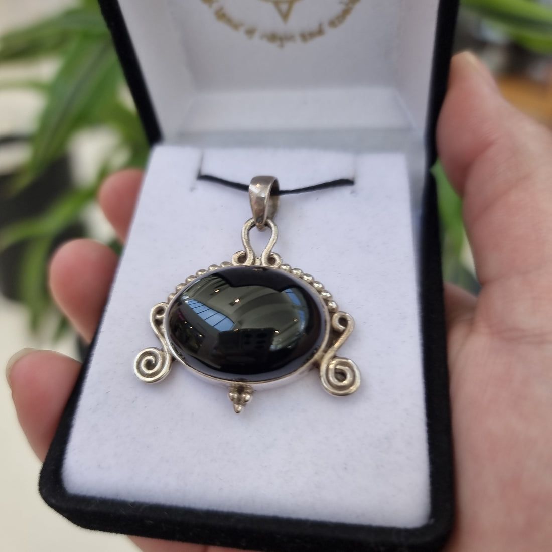 Close view of an oval black onyx pendant with silver scrollwork inside an open jewellery box