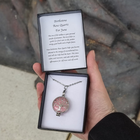 Hand holding an open black gift box with a rose quartz Tree of Life pendant on a chain and a card reading Birthstone Rose Quartz For June