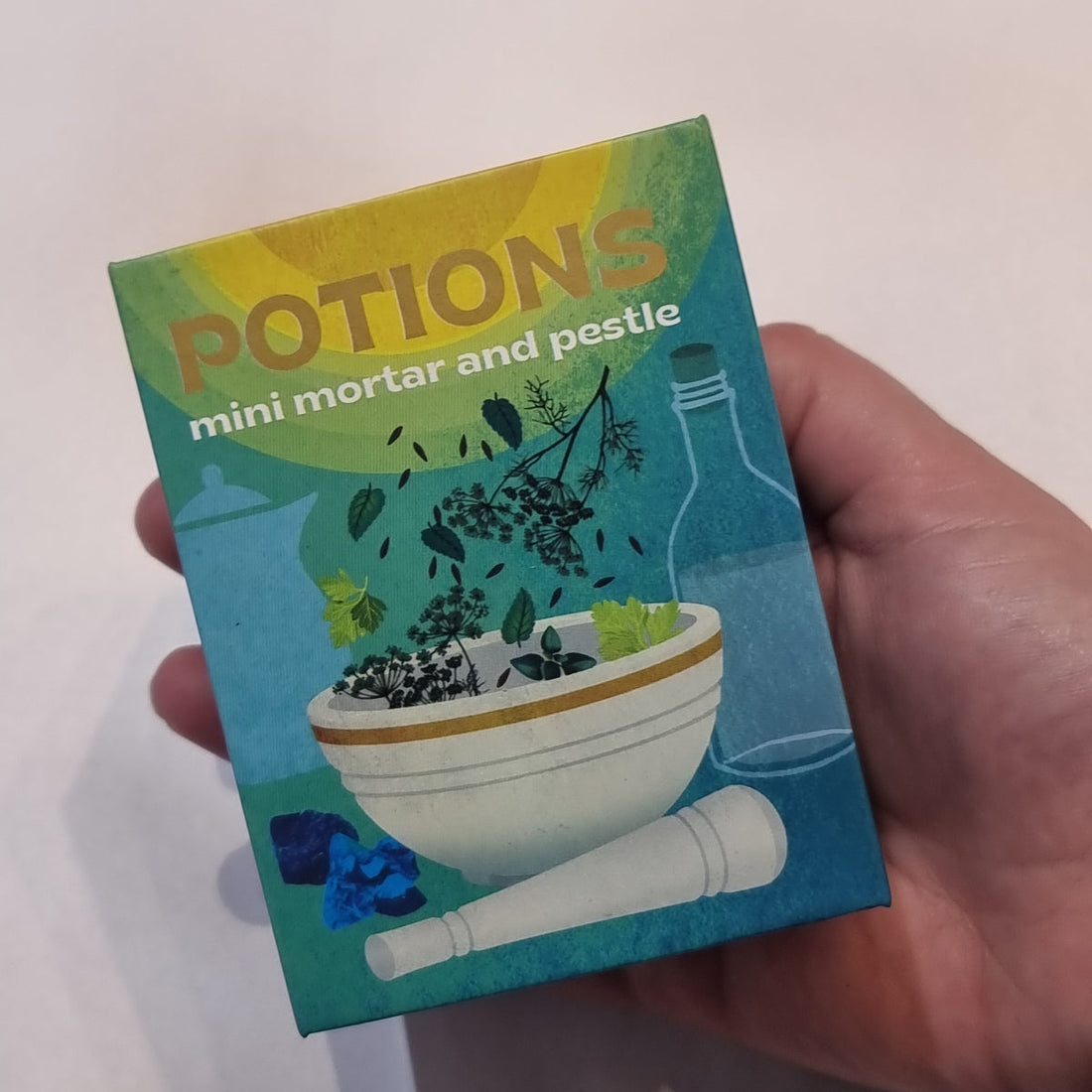A Potions mini mortar and pestle kit box, illustrated with a white mortar, herbs and bottles, held in one hand