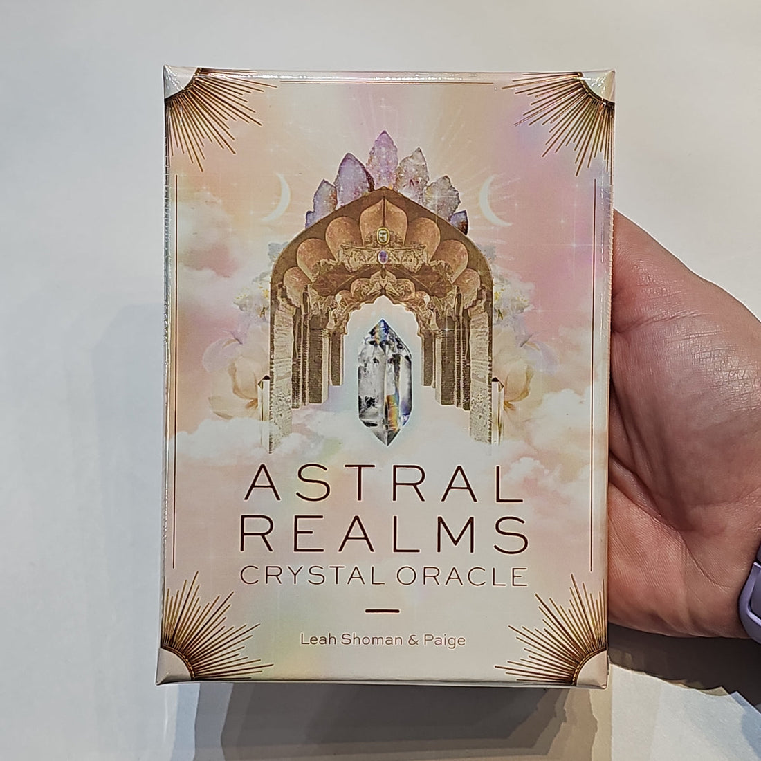 Hand holding the Astral Realms Crystal Oracle box, its pale arch of quartz points catching the light