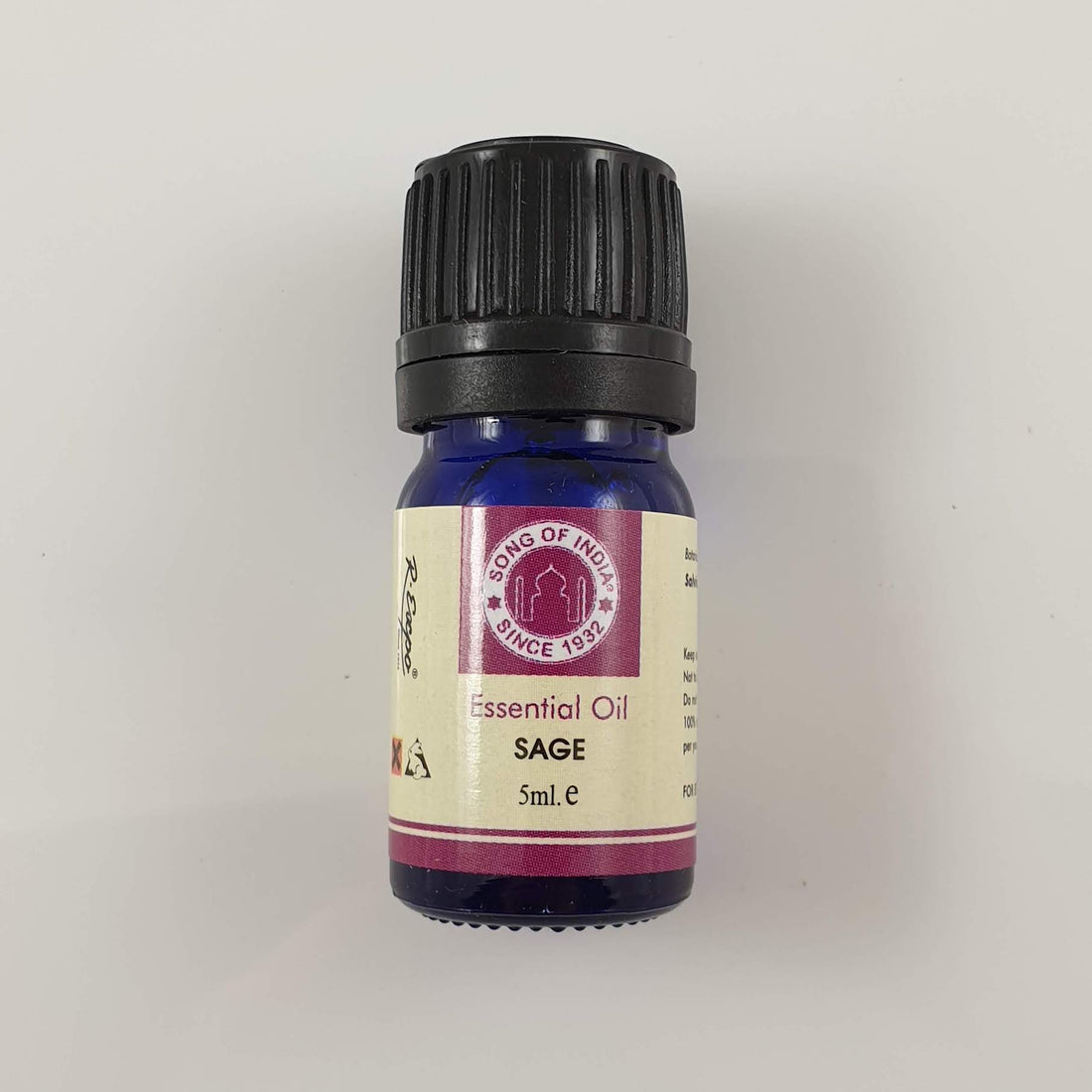 A cobalt-blue Song of India Sage essential oil bottle with a black cap and cream label on a pale grey surface