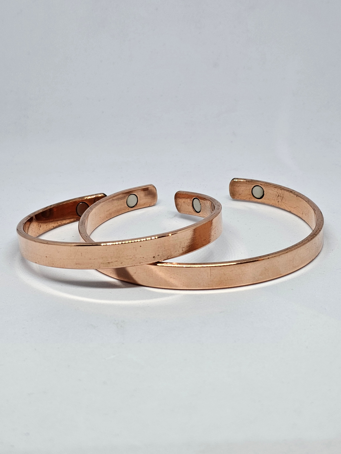 Three polished pure copper magnetic cuff bracelets on a pale background