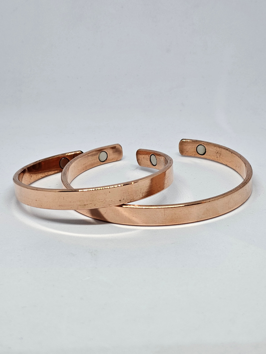 Three polished pure copper magnetic cuff bracelets on a pale background