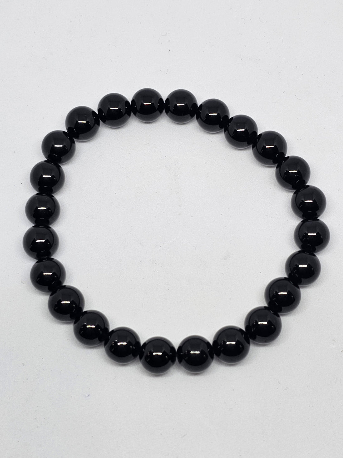 Black tourmaline round bead bracelet laid in a circle on a pale surface