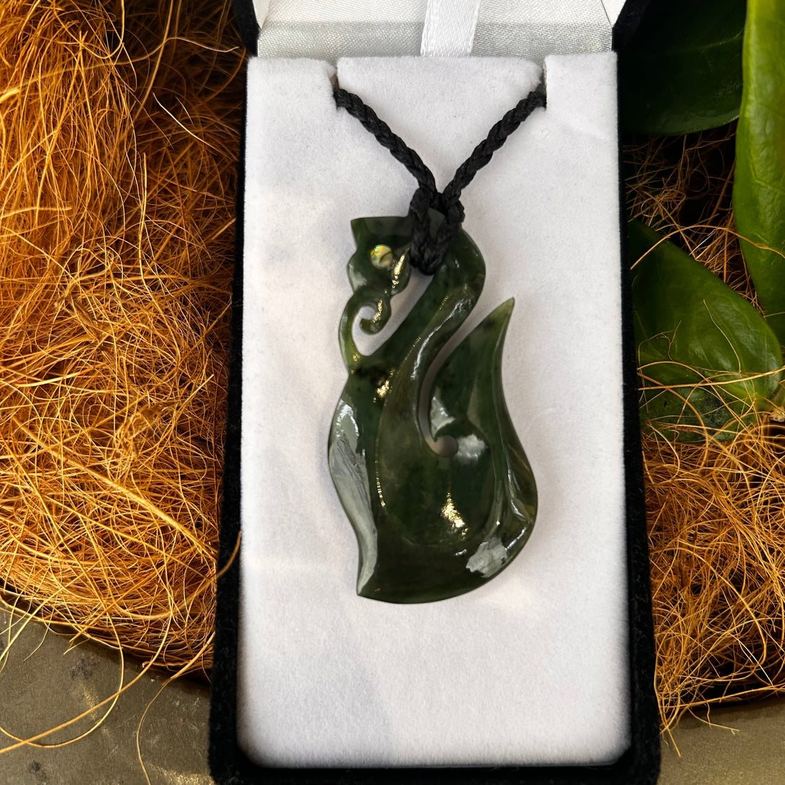 Carved greenstone manaia pendant with pāua shell eyes in a white velvet gift box