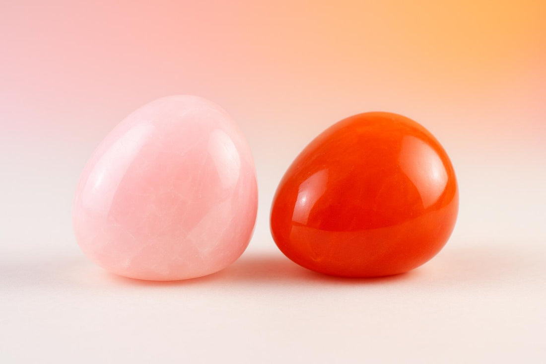 A polished pink rose quartz stone beside a warm orange-red carnelian stone on a soft pink and peach background