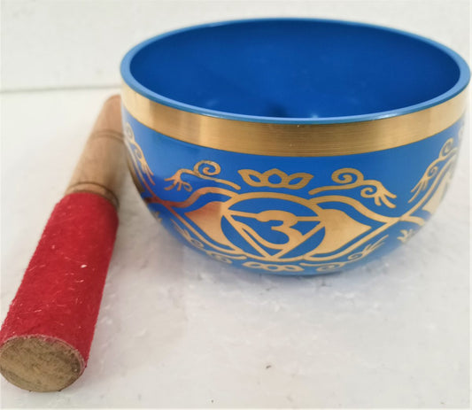 Blue singing bowl engraved with the gold third eye chakra symbol, beside a red suede striker