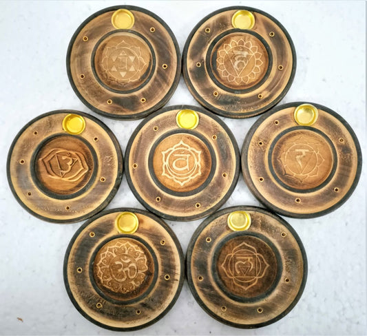 Seven round wooden incense holders, each carved with a different chakra symbol, laid out on a white table