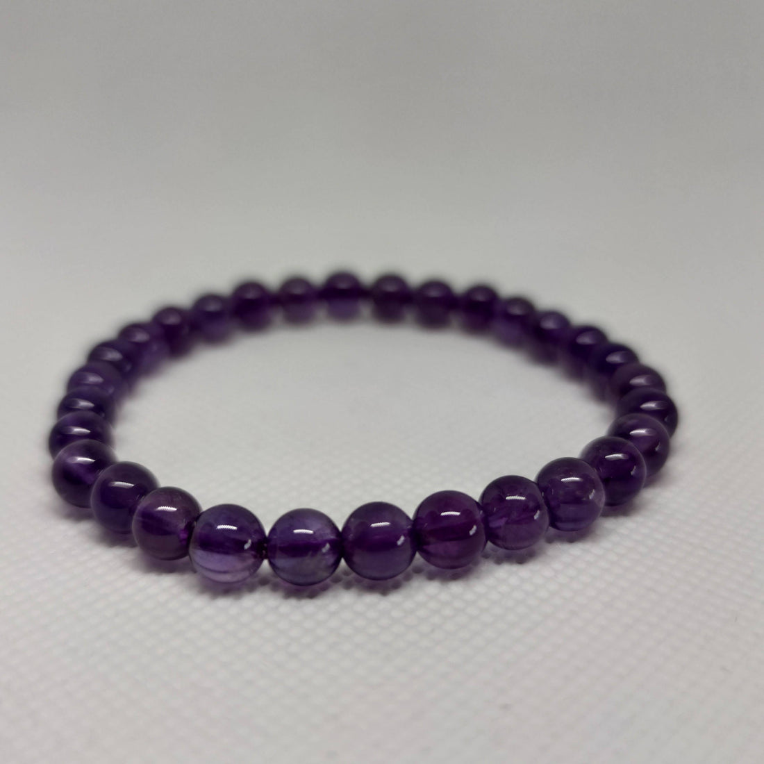 A round-bead amethyst crystal bracelet in soft violet tones resting on a pale surface