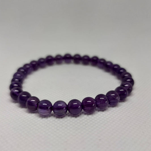 A round-bead amethyst crystal bracelet in soft violet tones resting on a pale surface