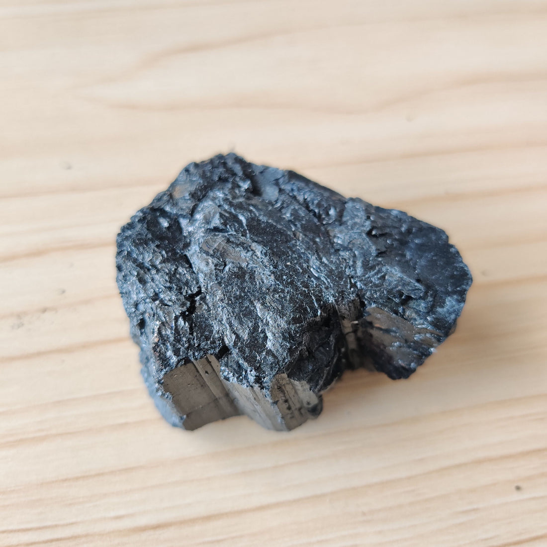 Rough black tourmaline crystal on a pale wooden surface