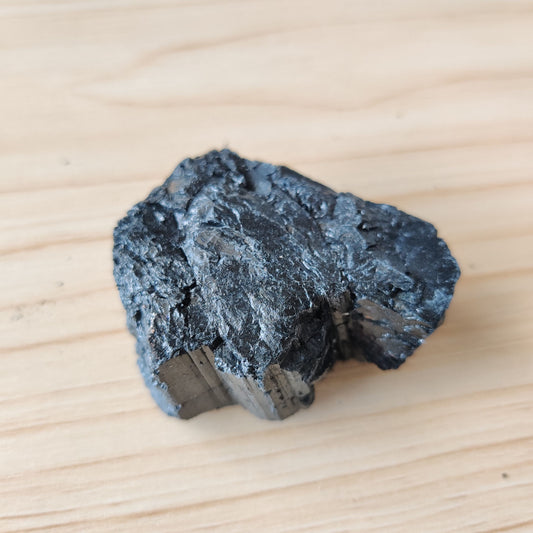 Rough black tourmaline crystal on a pale wooden surface
