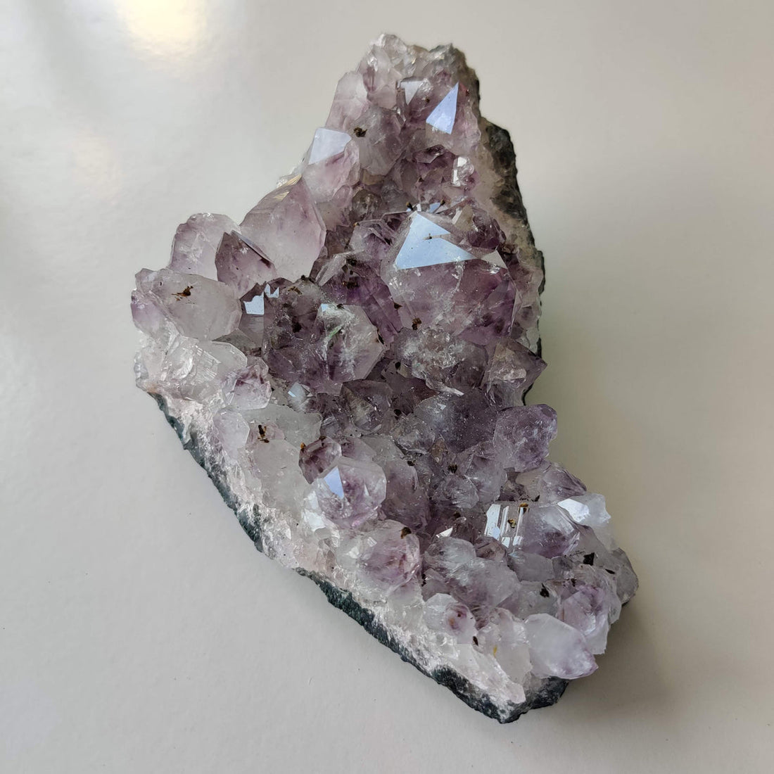 A natural amethyst crystal cluster with deep violet points, resting on a pale surface in soft light