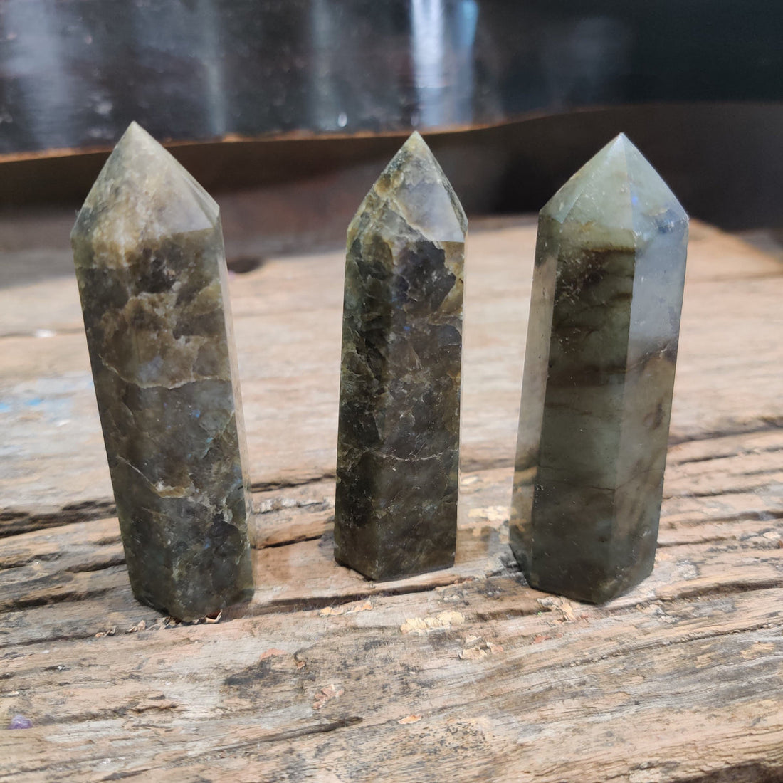 Three polished labradorite crystal points standing on a weathered wooden table
