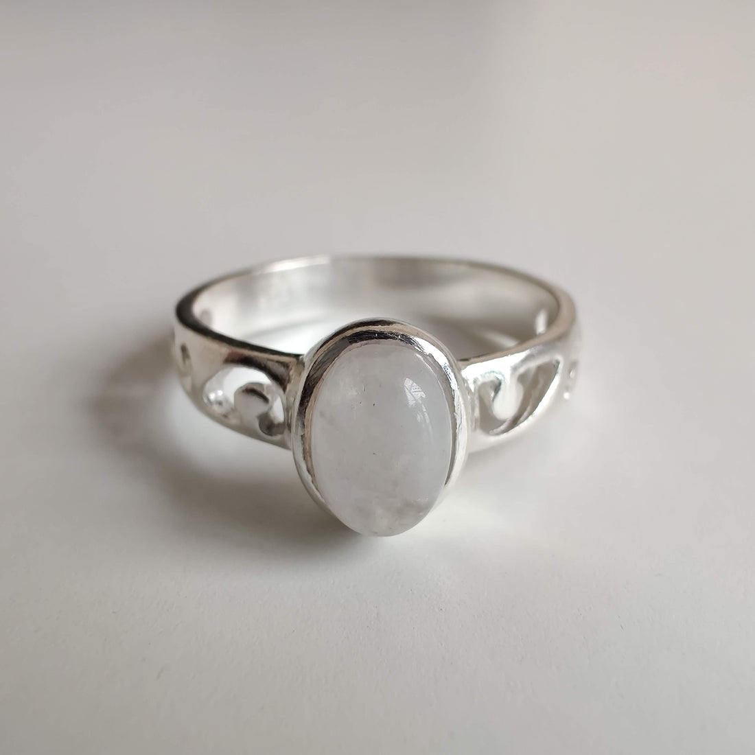 An oval moonstone set in a 925 sterling silver ring with a carved koru band on a pale surface