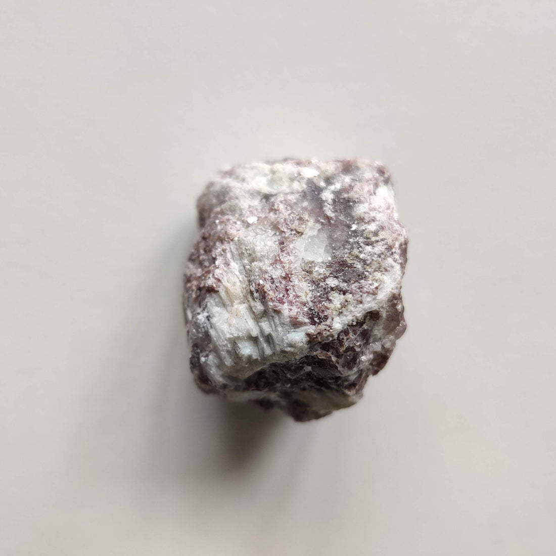 Raw lepidolite crystal piece, mauve and pale grey with a faint glitter, on a soft pale background