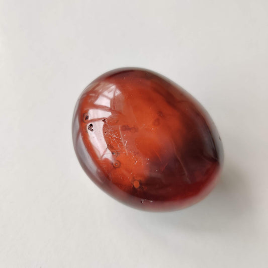 Polished carnelian palm stone showing warm orange and deep red banding