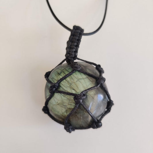A polished labradorite pendant on a cord, its grey stone flashing blue-green in the light
