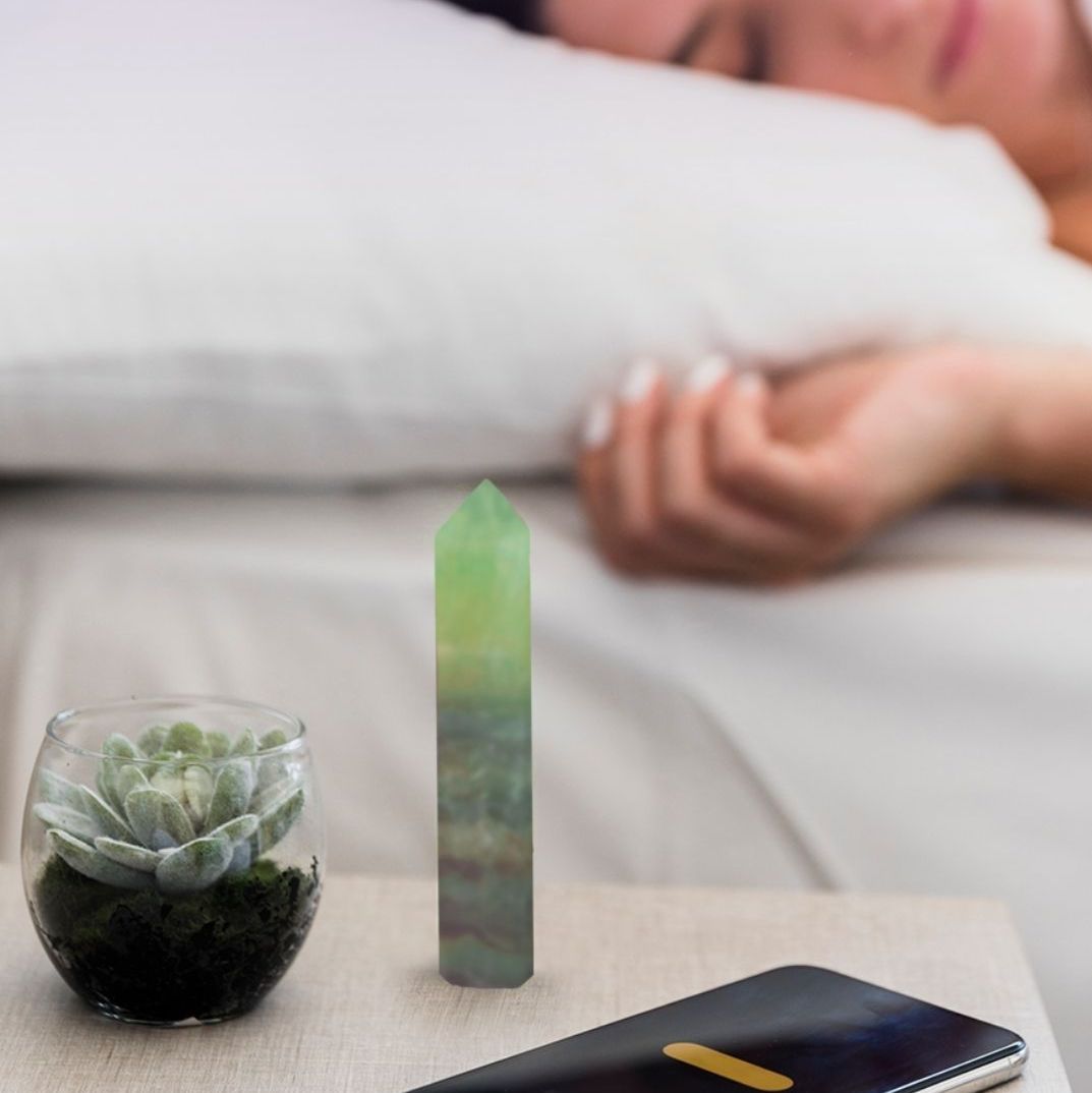 Person asleep on a white pillow beside a bedside table holding a green fluorite tower and a small succulent