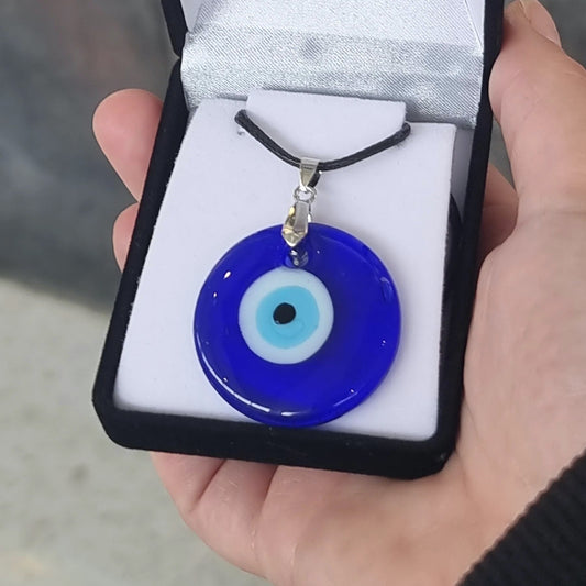 Hand holding a cobalt-blue glass nazar pendant in an open black gift box