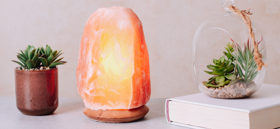 Glowing Himalayan salt lamp between two small succulents and a white book