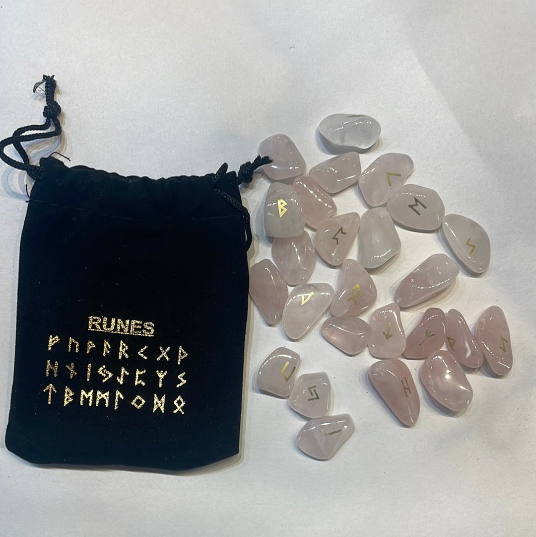 Pale pink rose quartz rune stones with gold symbols beside a black velvet pouch printed with the rune row