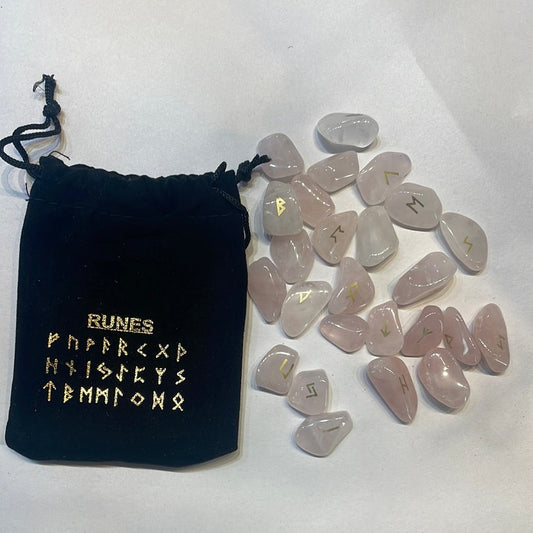 Pale pink rose quartz rune stones with gold symbols beside a black velvet pouch printed with the rune row