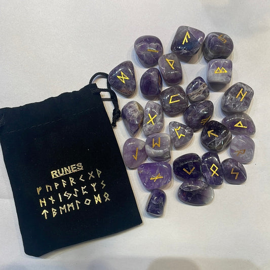 Purple amethyst rune stones with gold symbols beside a black velvet pouch printed with the rune row