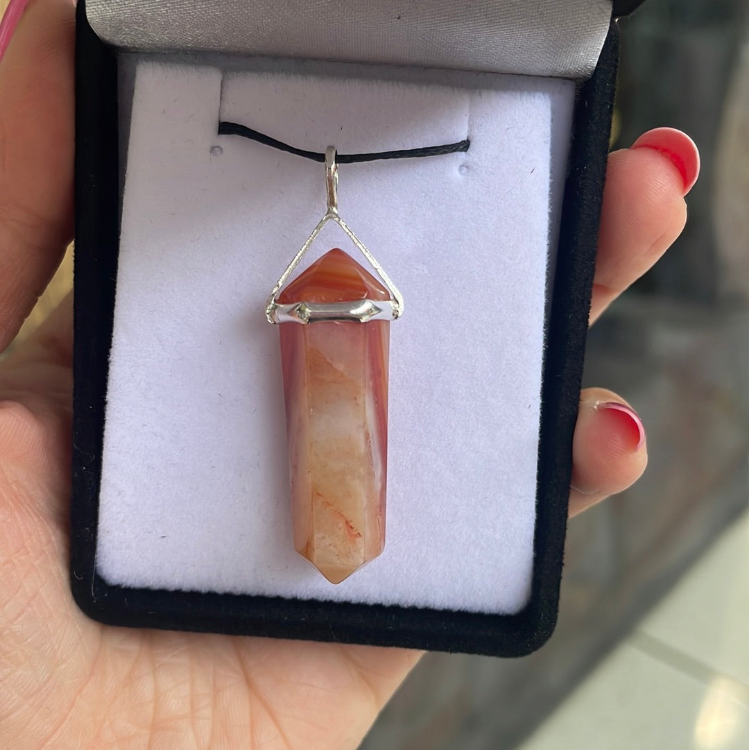 Hand holding an open black gift box with a carnelian point pendant set in silver on a black cord