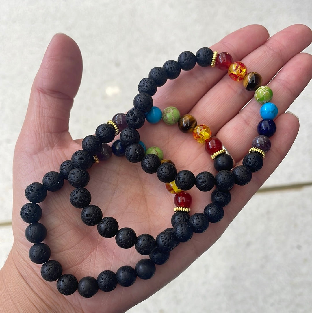 Three black lava bead bracelets with seven coloured chakra beads held in an open palm