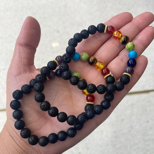 Three black lava bead bracelets with seven coloured chakra beads held in an open palm