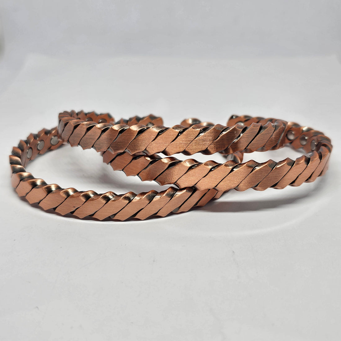 Three plaited copper cuffs stacked together on a white surface