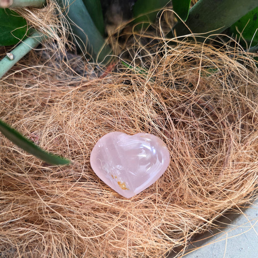 A small pink rose quartz heart resting in a nest of soft coconut fibre